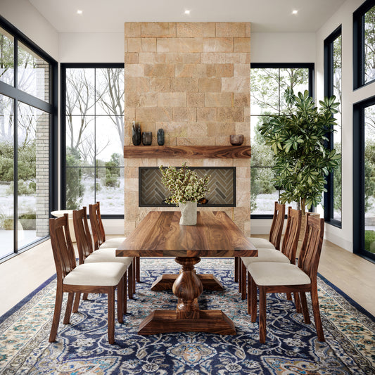 A elegant dining table with wooden legs and a rectangular shape, placed in a room with a fireplace and large windows, with chairs around it and a patterned rug underneath.