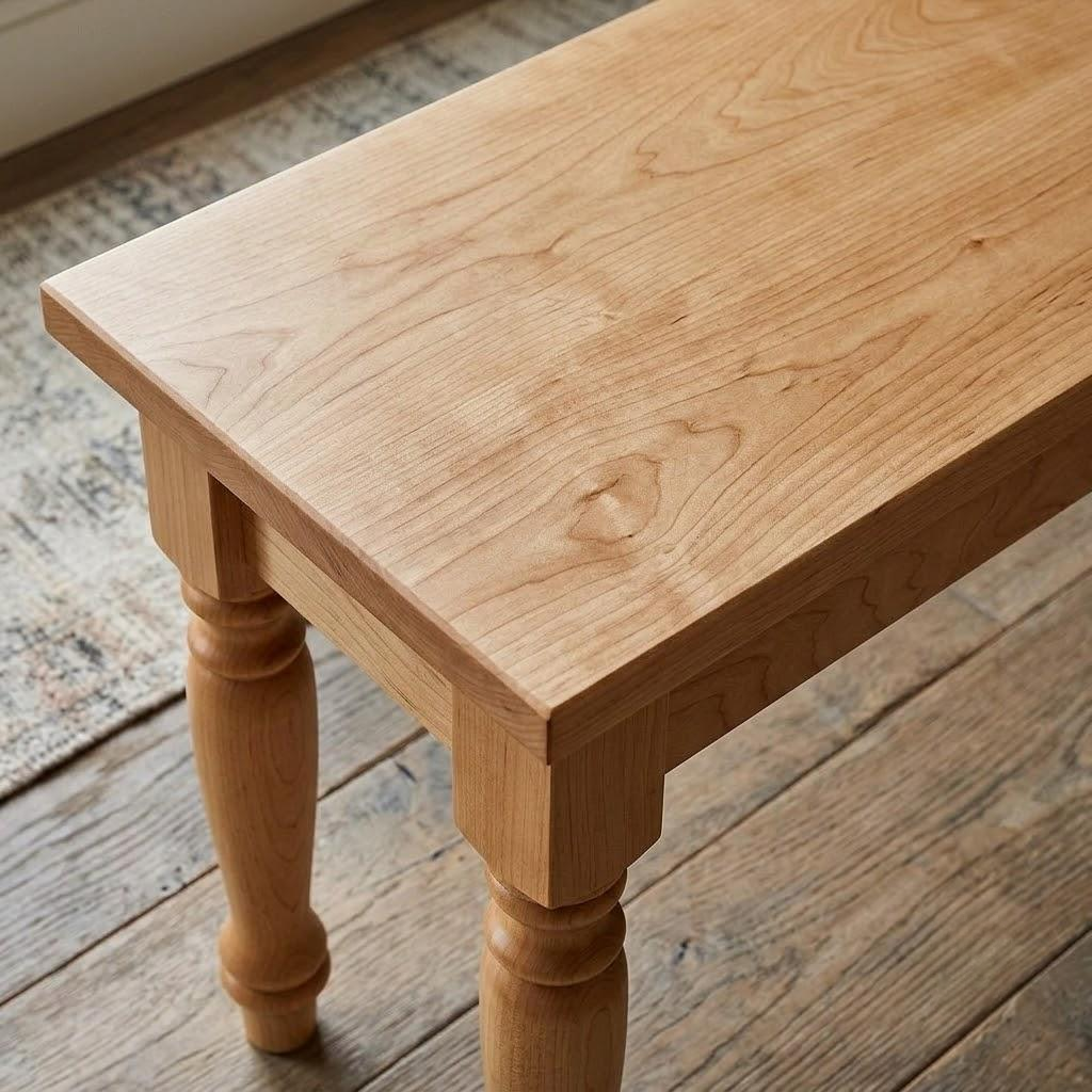 A close-up of a light natural wood table or bench with turned legs, shown on a rustic wooden floor and patterned rug.