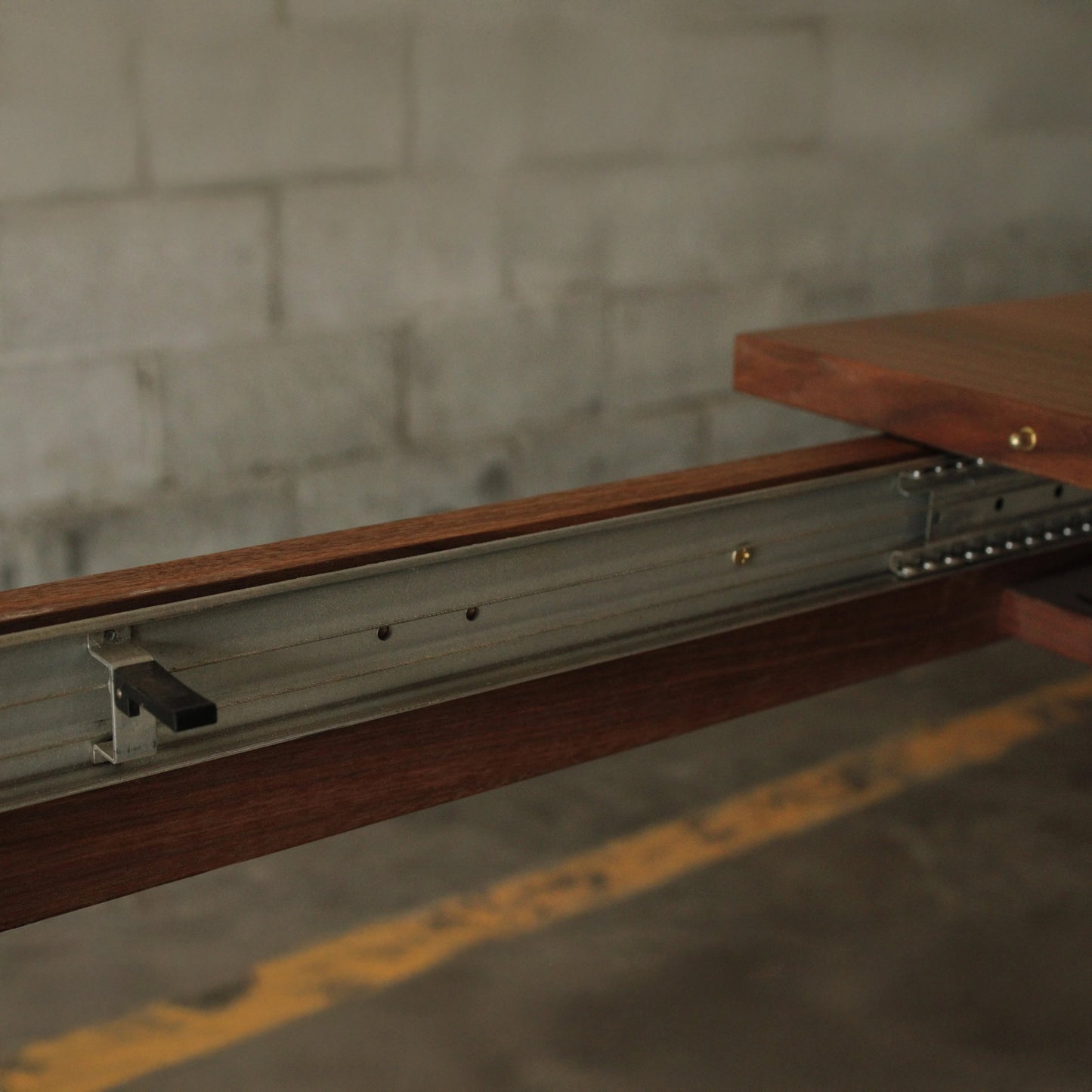 A rectangular dining table with a dark wood finish and metal legs, placed on a concrete floor against a brick wall.