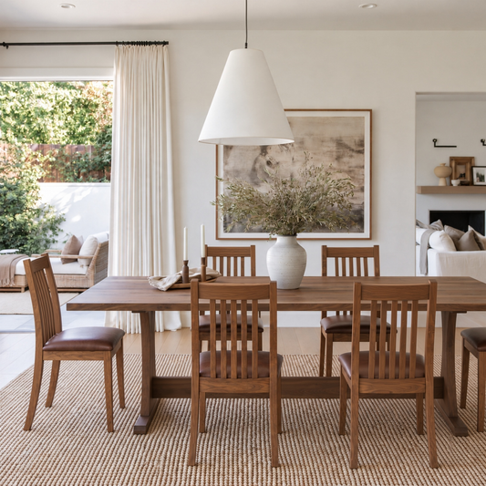 Side view of the Walnut Rowland Dining Table with Ensworth Chairs, highlighting the solid walnut tabletop, trestle base, and warm wood tones in a bright dining space.