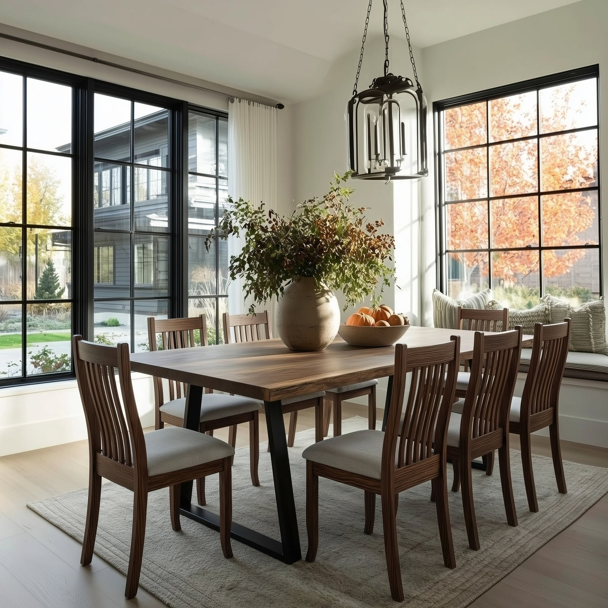 Dining room with wooden table and chairs, large windows, and a vase of flowers.