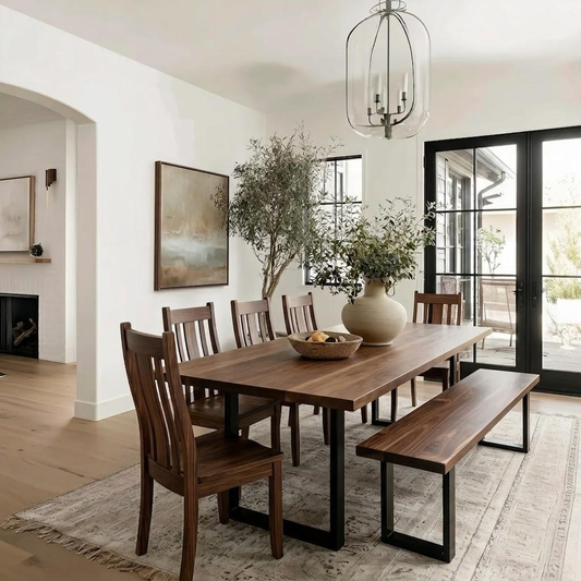 A dark wood dining table with matching chairs and a bench in a bright, modern dining room. The table has a rectangular shape with a smooth dark wood grain, supported by black metal legs.