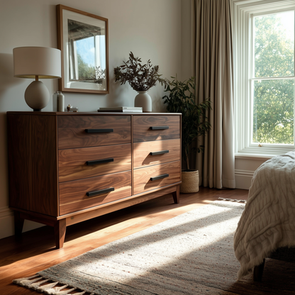 Wooden dresser in a bedroom with a lamp, mirror, and plants.