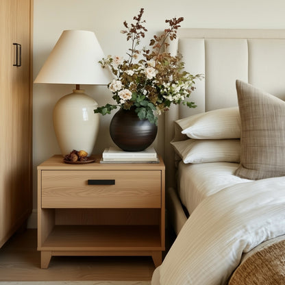 Wooden nightstand with lamp and decor next to a bed in a bedroom.