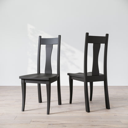 Two black wooden dining chairs with, one in front of the other, against a white background.