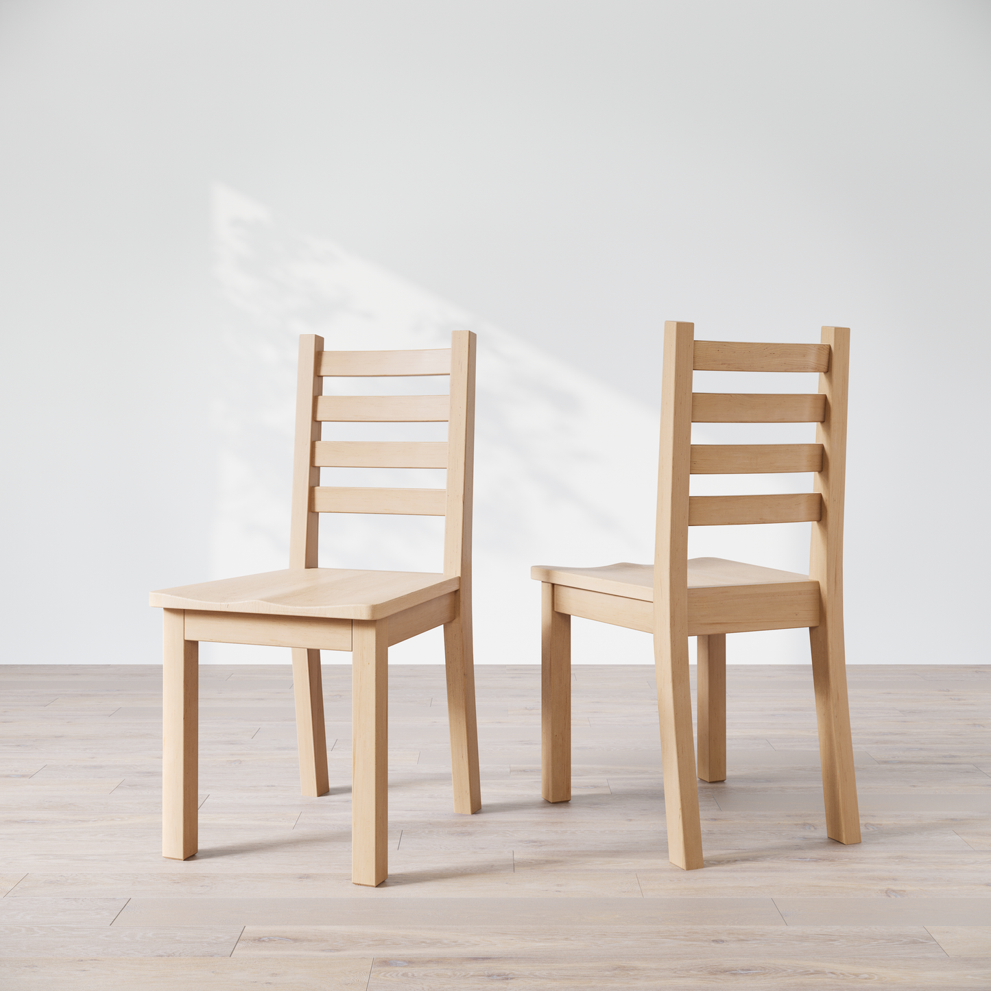 Two wooden dining chairs with a natural finish, with a ladder back design, placed side by side on a bright floor against a white wall.