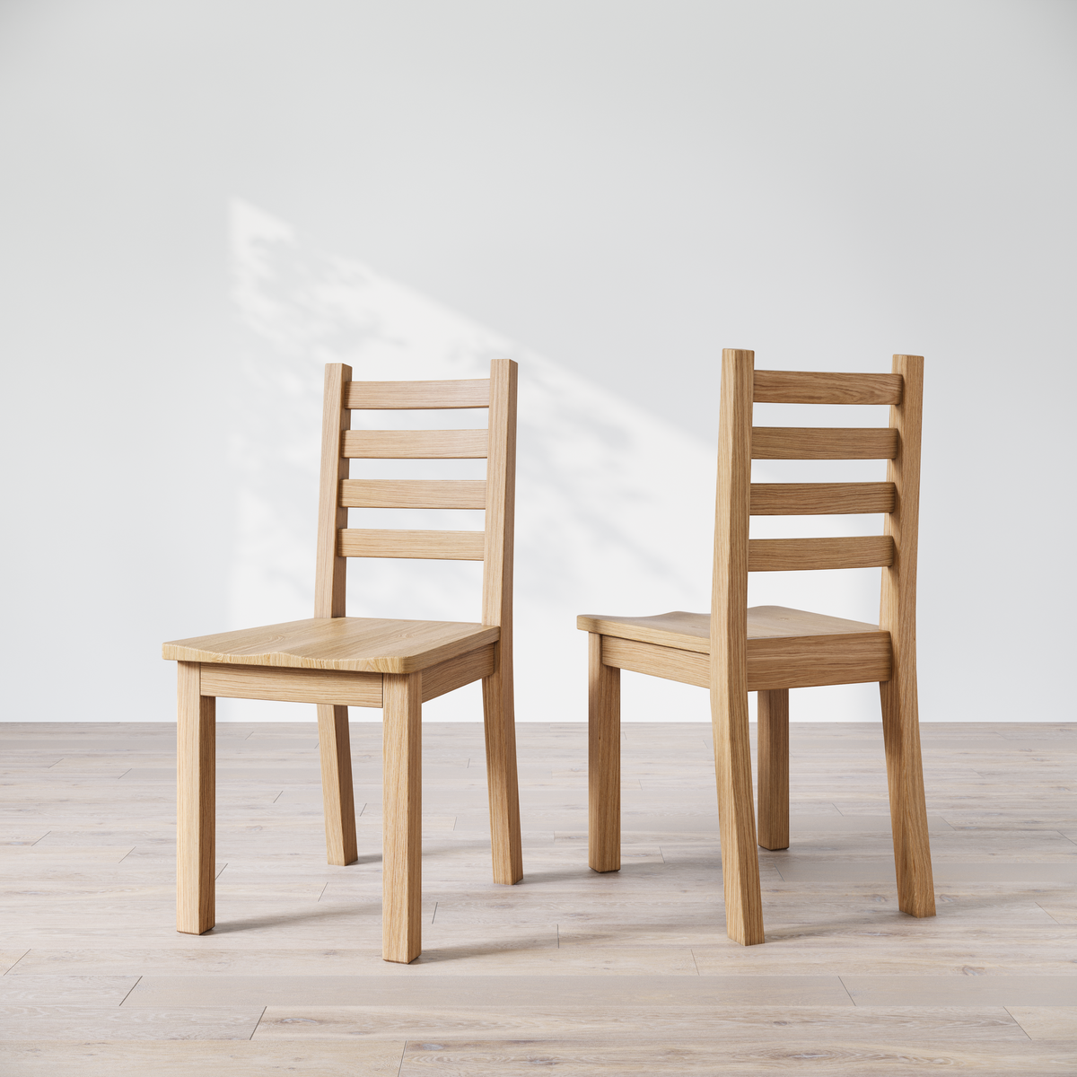 Two oak wood Coleman dining chairs with a natural finish, with a ladder back design, placed side by side on a bright floor against a white wall.