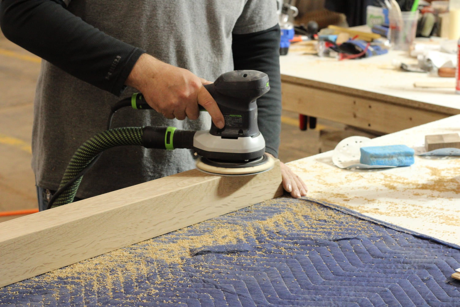 Person sanding a wooden surface with a sander in a workshop setting