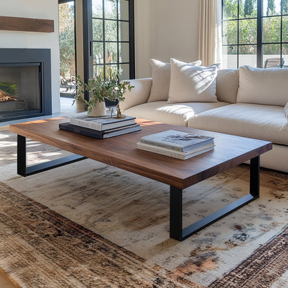 A rectangular Underhill Walnut Coffee Table with black steel legs, placed on a patterned rug in a living room setting, featuring items on top such as books and a plant.