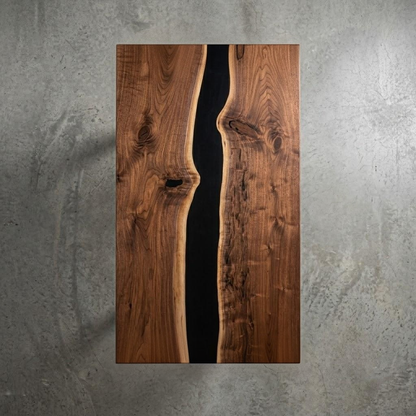 A rectangular wooden wall art panel with a live edge design, featuring two warm brown wood planks meeting in the center with a dark black resin channel, displayed against a textured gray concrete wall.