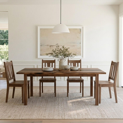 A rectangular wooden dining table with four matching wooden chairs, styled in a bright, modern dining room with a white pendant light, a large framed abstract print, and a woven area rug.