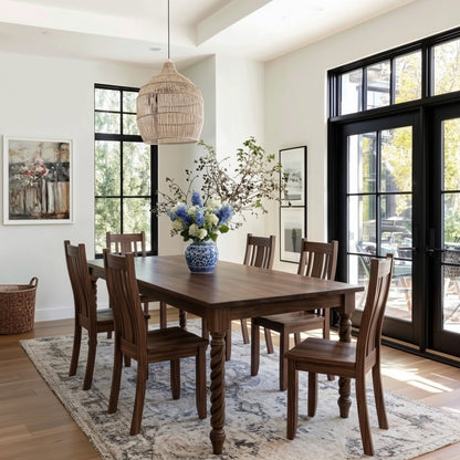 Dining room with wooden table and chairs, vase of flowers, and large windows.