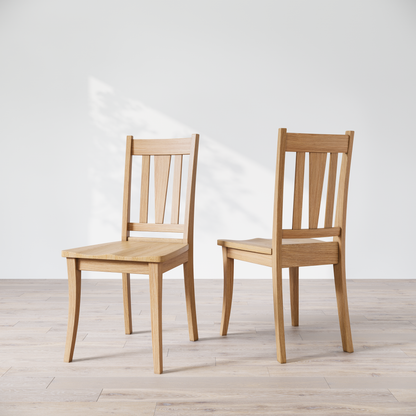 Two oak dining chairs with a brown finish, showcasing a slatted backrest and a solid seat, placed against a white background.