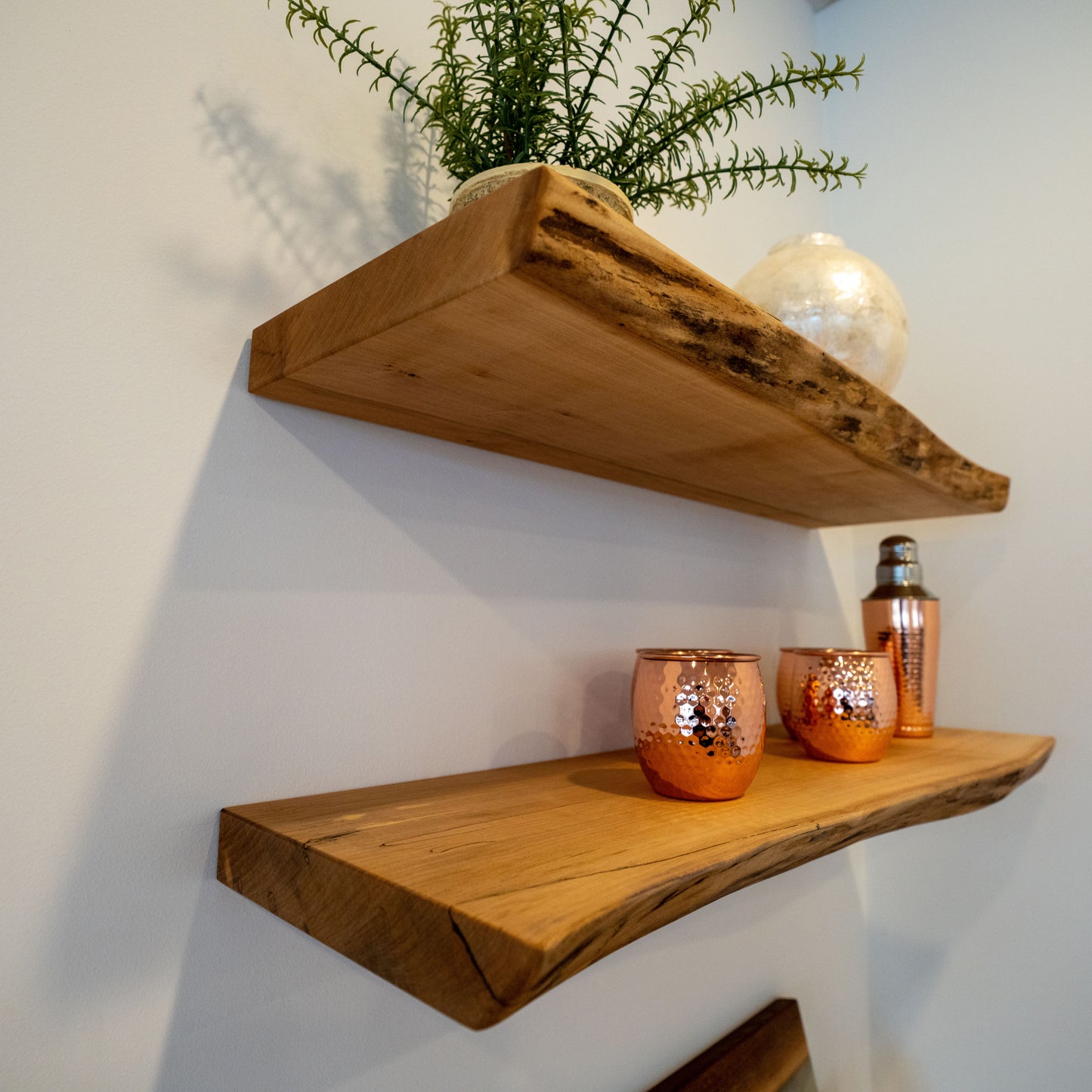 Two live edge maple shelves mounted on a wall, with decorative items and plants displayed on them.