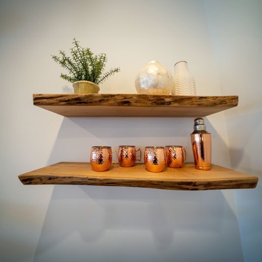 Two live edge maple shelves mounted on a wall, with decorative items and plants displayed on them.