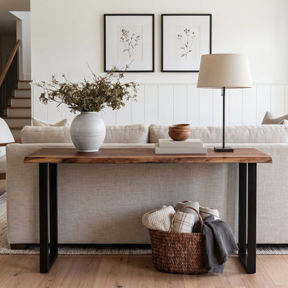 A rustic farmhouse-style console table with a live-edge medium brown wood top and black metal legs, styled in a bright living room setting.