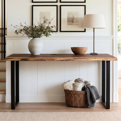 A rustic farmhouse-style console table with a dark wood top and black metal legs, styled in a bright home entryway with a vase, bowl, lamp, framed art, and a basket underneath.
