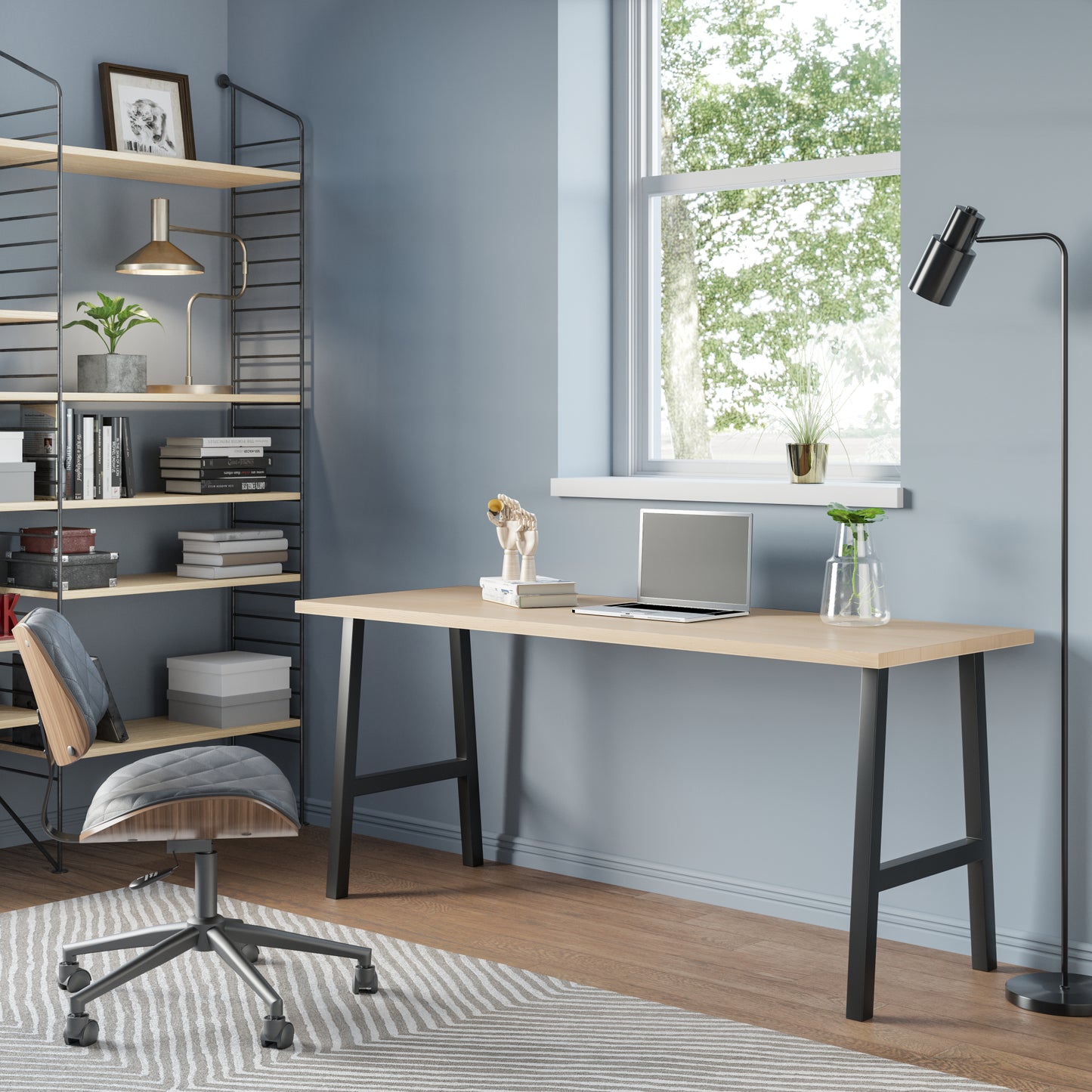 A sleek modern desk with a wooden top and black metal legs, situated in a well-lit room with a chair pulled up to it. Decorative items and a framed picture hang on the wall in the background.