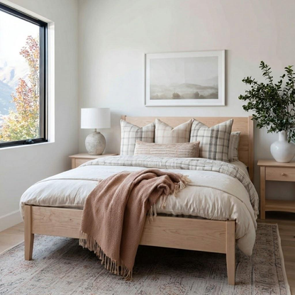 Neatly made bed with wooden headboard in a bright bedroom with a window and decor.