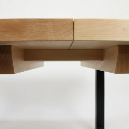 Wooden dining table with end extensions and black metal legs on a white background