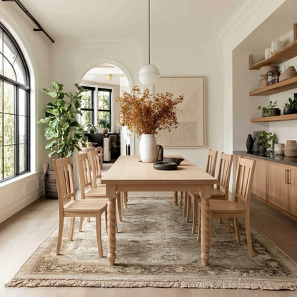 Dining room with wooden table and chairs, floral arrangement, and large windows.