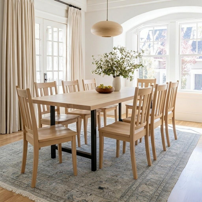 Dining room with wooden table and chairs, large windows, and a vase of flowers.