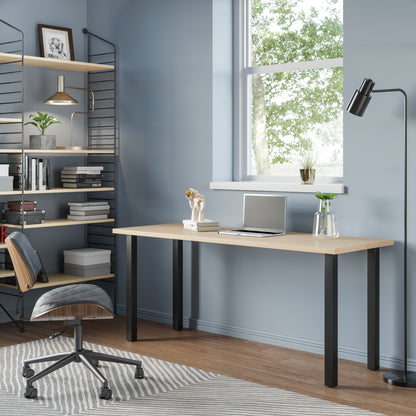 A sleek modern desk with a wooden top and black metal legs, situated in a well-lit room with a chair pulled up to it. Decorative items and a framed picture hang on the wall in the background.