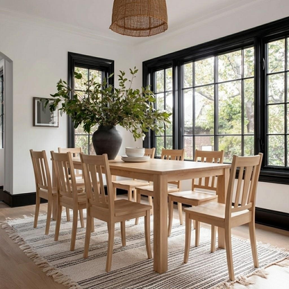 Dining room with wooden table and chairs, large windows, and a vase with plants.