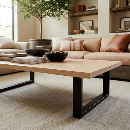 A modern rectangular coffee table with a light natural wood top and black metal U-shaped legs, styled in a warm, contemporary living room setting.