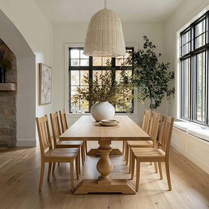 Dining room with wooden table and chairs, large windows, and decorative plants.