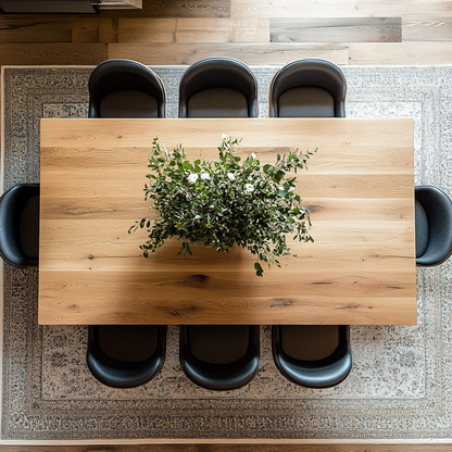 A elegant dining table with wooden legs and a rectangular shape, placed in a room with a fireplace and large windows, with chairs around it and a patterned rug underneath.