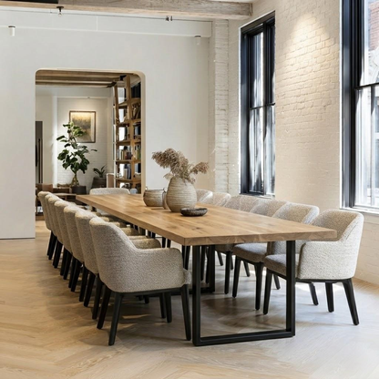 Long wooden dining table with chairs in a modern room with large windows and brick wall.