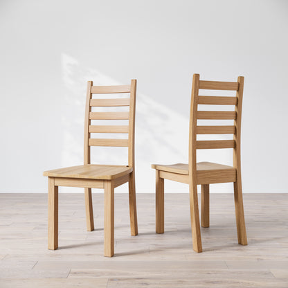 Two oak wood Heisly dining chairs with a commercial grade finish, displayed against a white background.