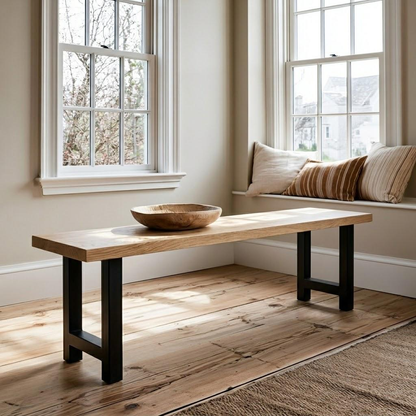A rustic wooden console table with a light oak top and black metal legs, styled in a bright room with a wooden bowl on top, set against a window and a cushioned window seat.