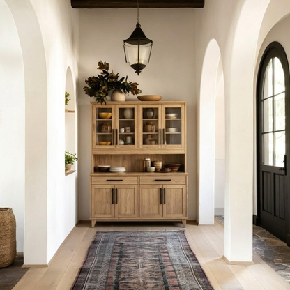 Wooden cabinet with decorative items in a bright room with arches and a rug.