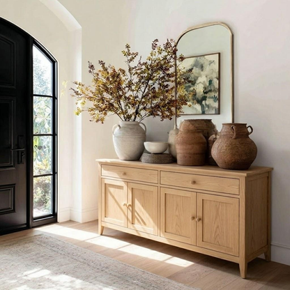 Wooden sideboard with decorative vases and a mirror in a bright room.