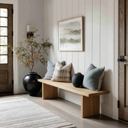 Nestled entryway with a wooden bench, decorative pillows, and a framed picture on a paneled wall.