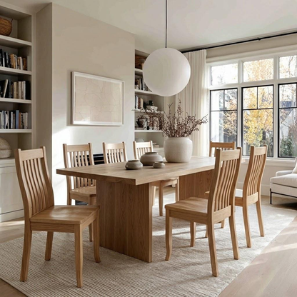 A light natural wood dining table with six matching slatted chairs, styled in a bright, modern dining room with a large white globe pendant light, bookshelves, and a window.