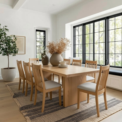 Dining room with wooden table and chairs in a bright room with large windows.