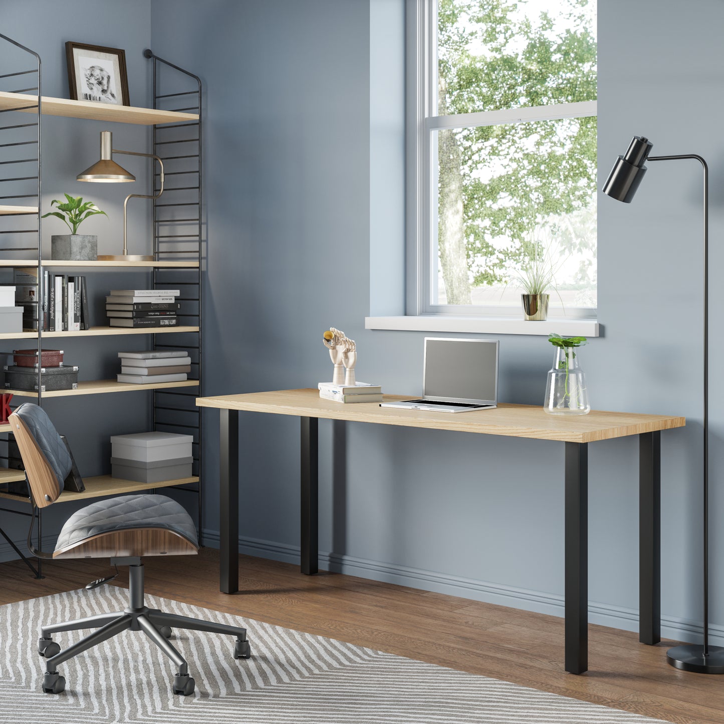A sleek modern desk with a wooden top and black metal legs, situated in a well-lit room with a chair pulled up to it. Decorative items and a framed picture hang on the wall in the background.