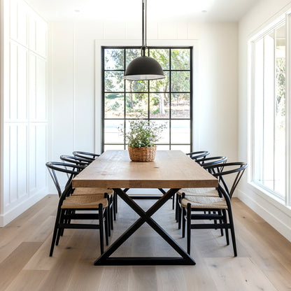 Oak dining table with black metal x legs in a well lit dining room with rattan chairs and large windows