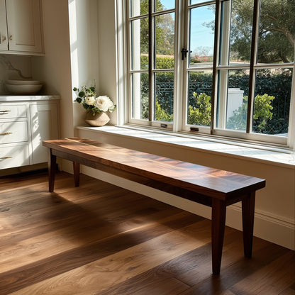 Wooden bench in a room with large windows and a view of greenery outside.