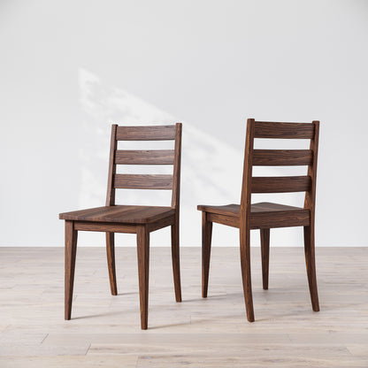 Two wooden dining chairs with a dark finish, featuring a simple, solid backrest and seat design on a light background.