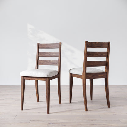Two wooden dining chairs with a dark finish and upholstered seats, featuring a simple, solid backrest on a light background.