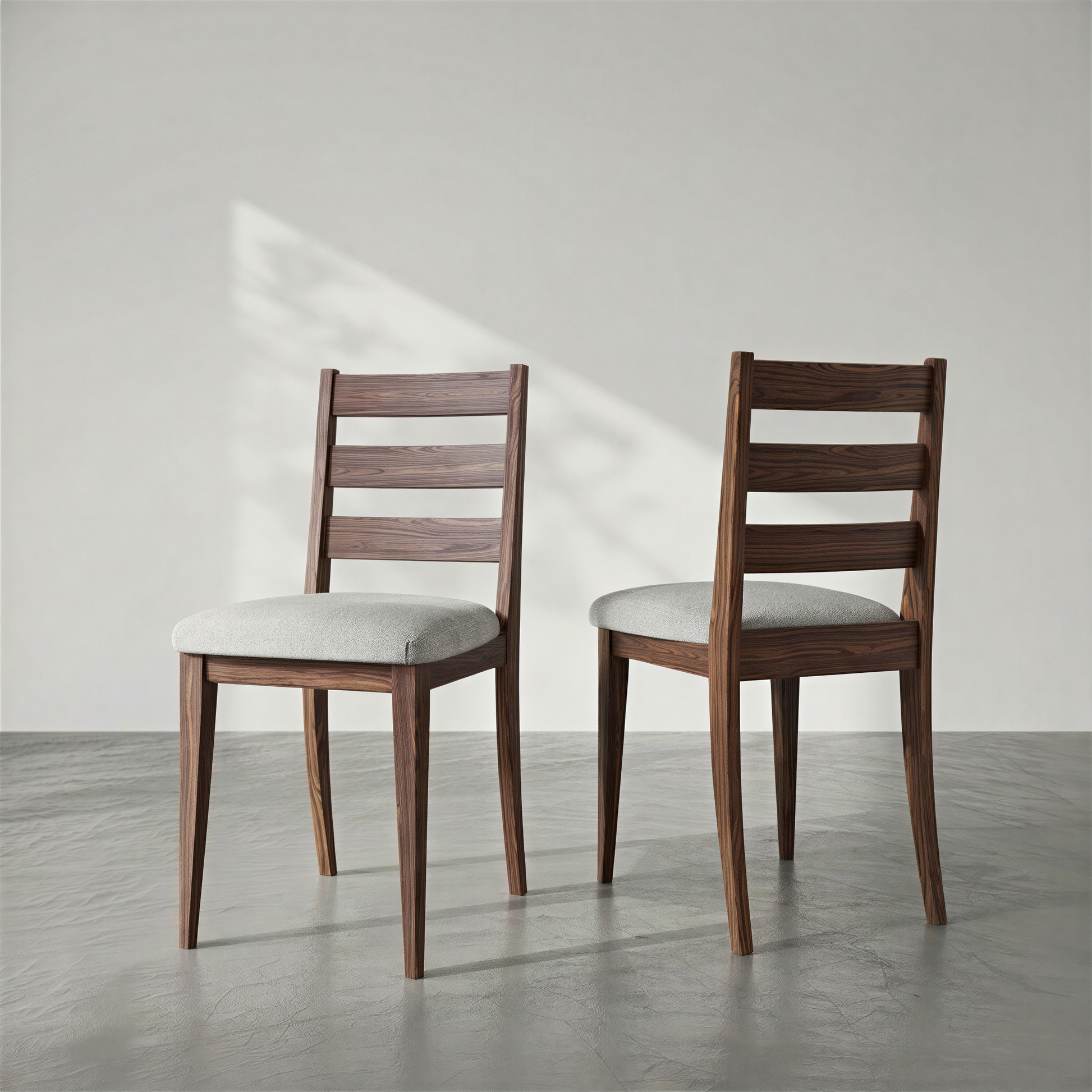 Two wooden chairs with white cushions on a gray floor and light gray wall.