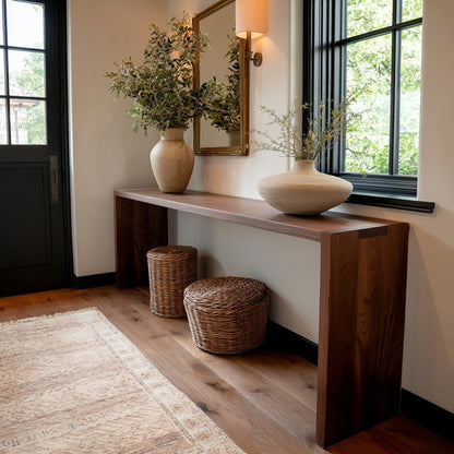 Wooden console table with decorative vases and plants in a room with large windows.