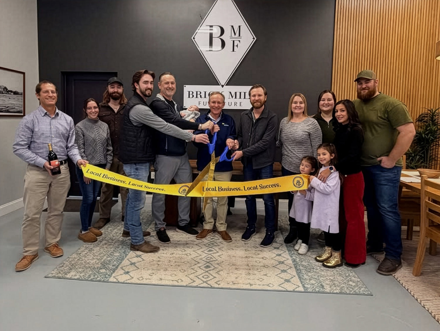 Group of people cutting a ribbon in a room with a logo on the wall.