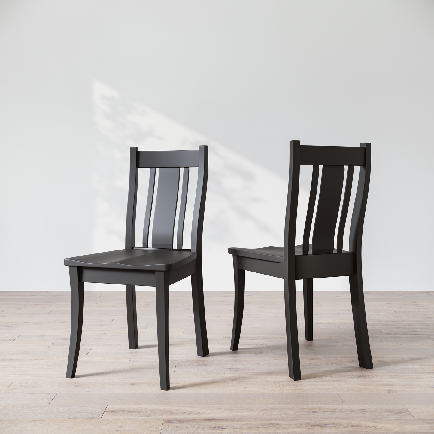 Two black wooden dining chairs with a full backrest, placed on a light grey floor against a white wall.