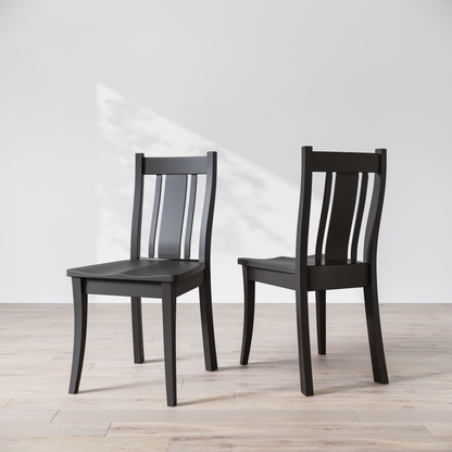 Two black wooden dining chairs with a full backrest, placed on a light grey floor against a white wall.