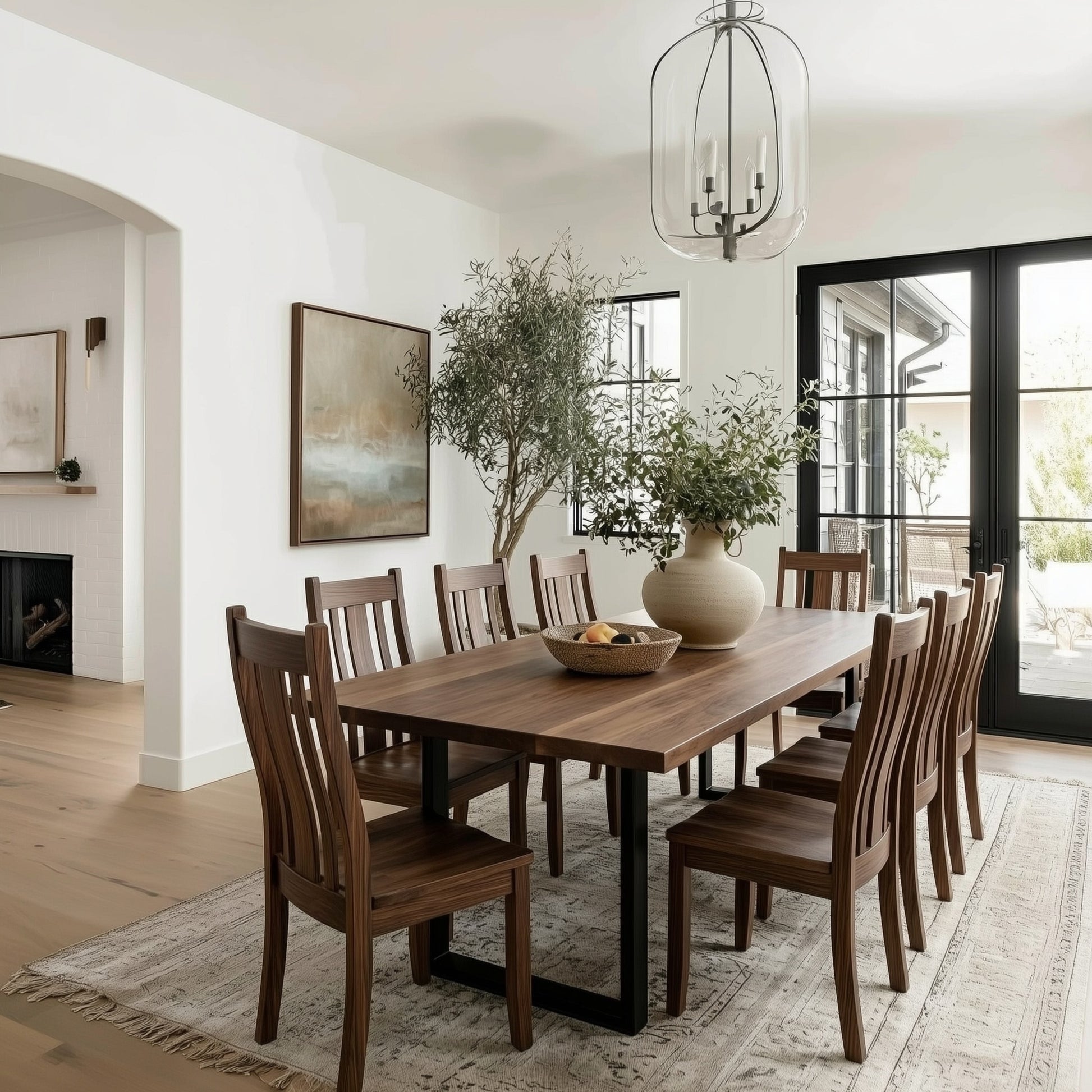 Dining room with wooden table and chairs, large windows, and a vase of flowers.
